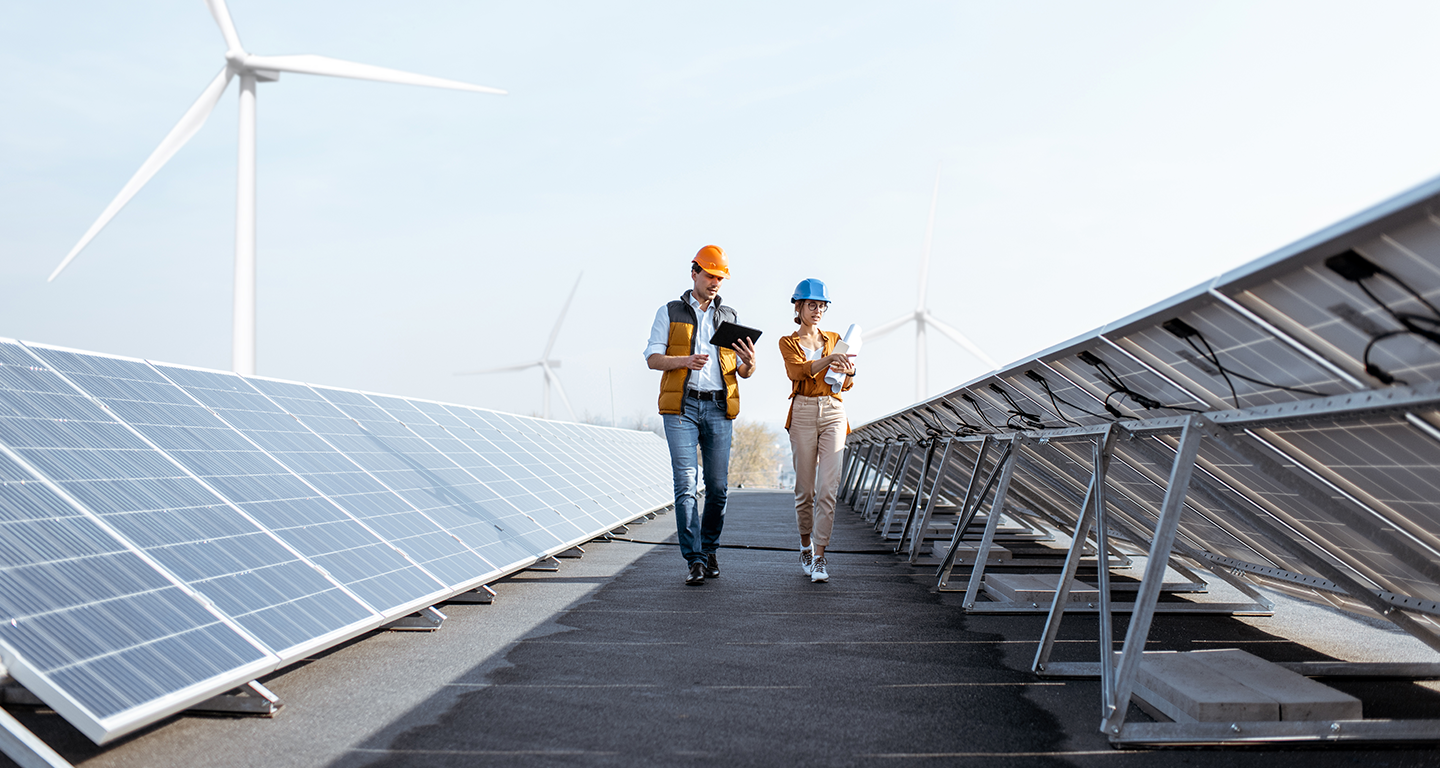 Profesionales inspeccionando instalación de paneles solares con turbinas eólicas al fondo - Energías renovables